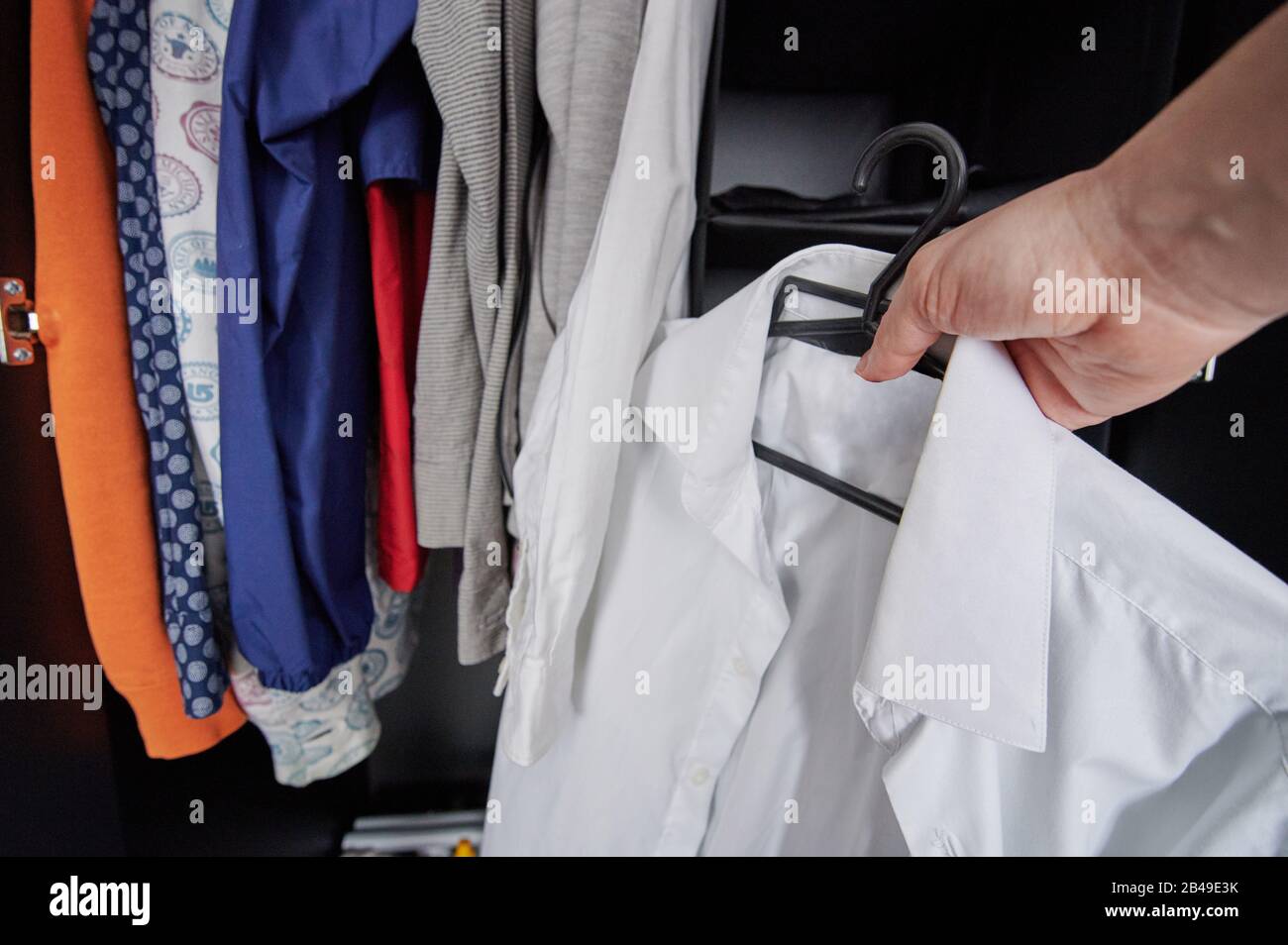Hand hold hanger with white shirt on wardrobe background Stock Photo