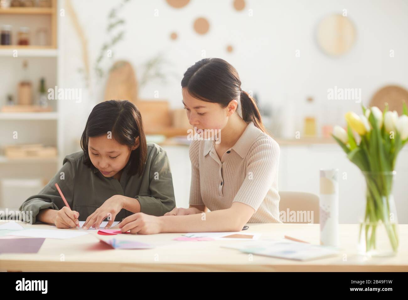 Two girls sitting together at table at home on sunny day creating ...