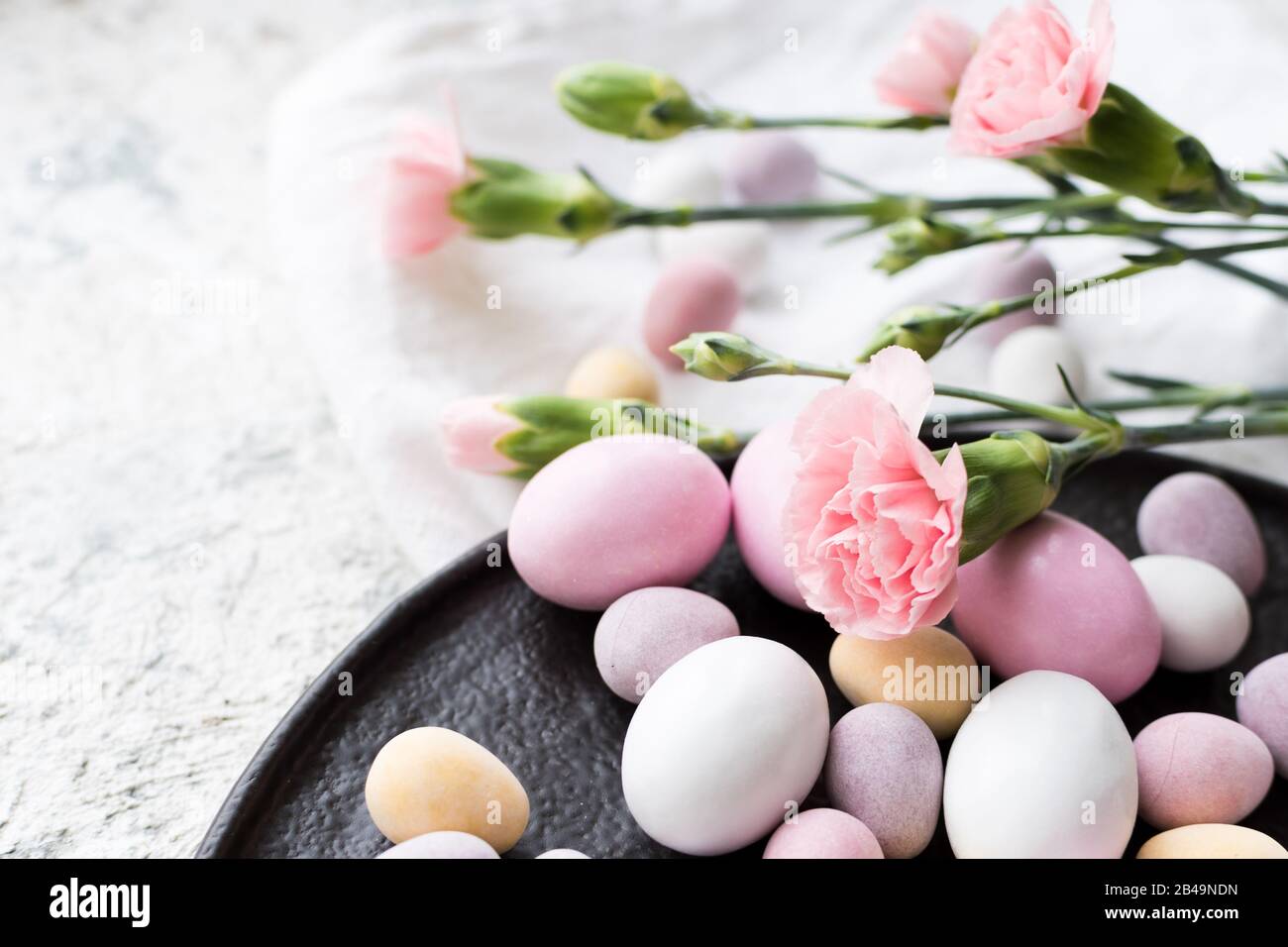 Easter composition with mini chocolate eggs in pastel colors and pink flowers on grey concrete background. Happy Easter Holidays. Stock Photo