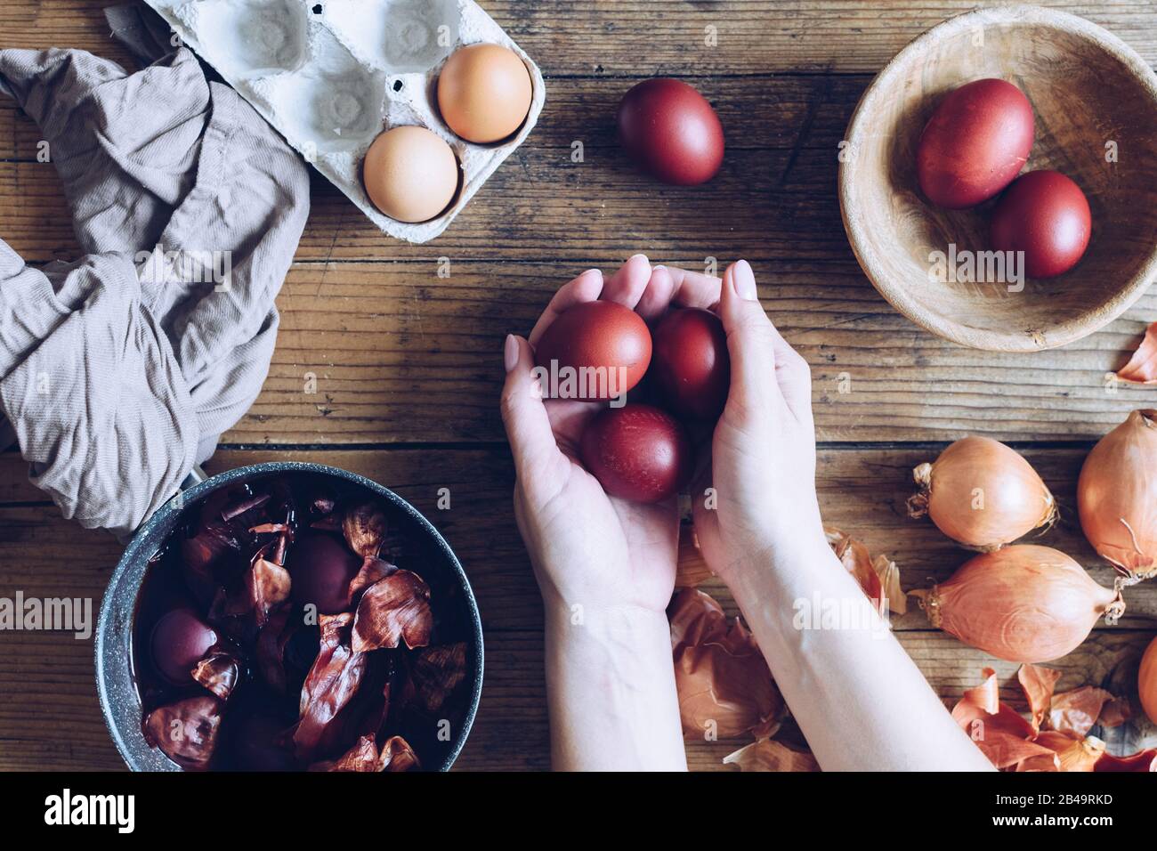 Woman making dyed Easter eggs painted with natural dye onion on wooden background. Process of dyeing eggs with natural paints for Easter. Natural ecol Stock Photo