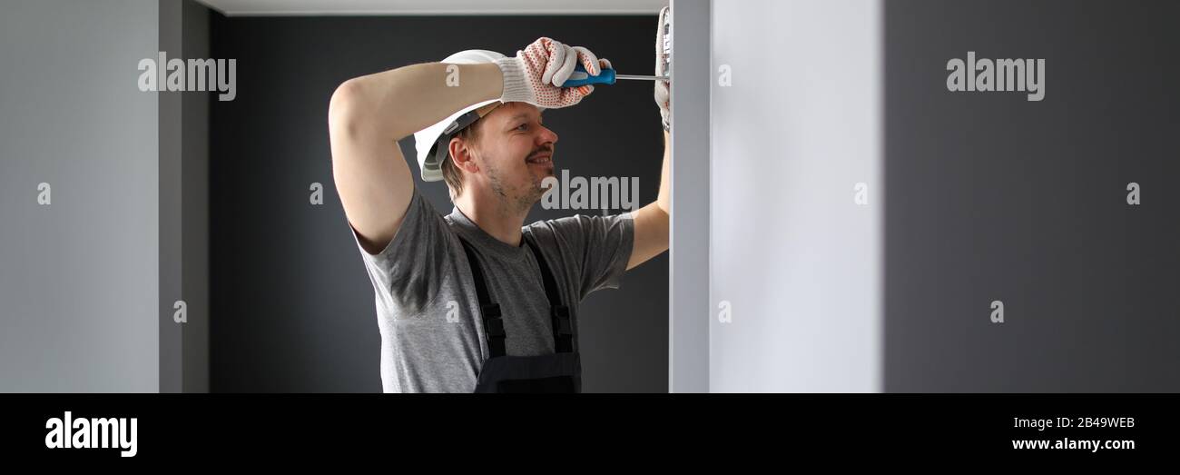 Young smiling repairman standing in empty flat and fixing electricity with screwdriver Stock Photo