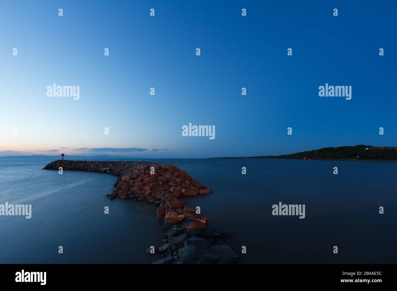 Jetty of rocks on the sjpre of Saint Lawrence river at blue hour. Canada Stock Photo