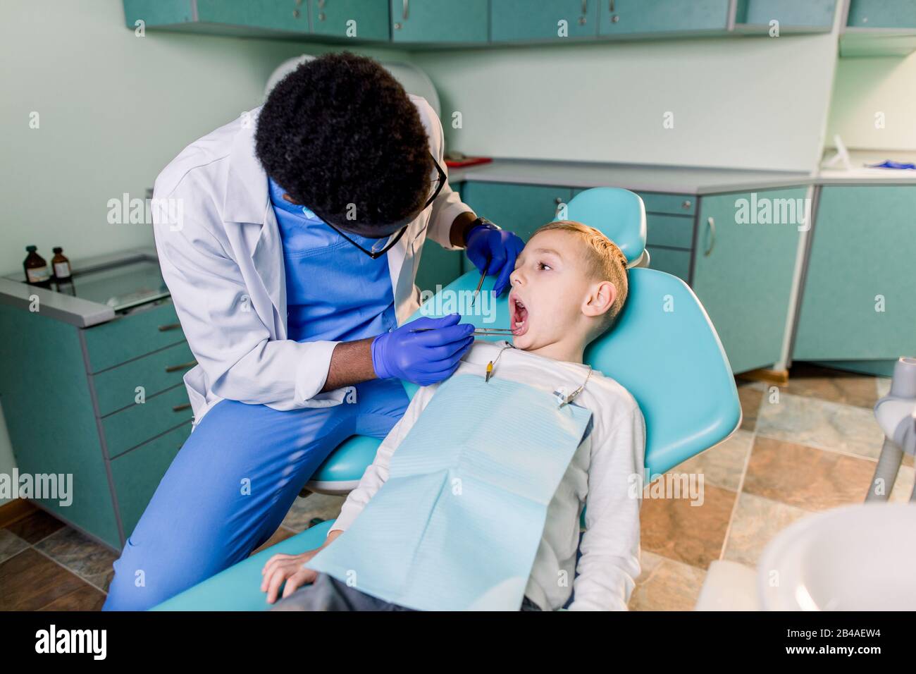 Young beautiful boy in dental office. Children's African-American dentist examines teeth to a child Stock Photo