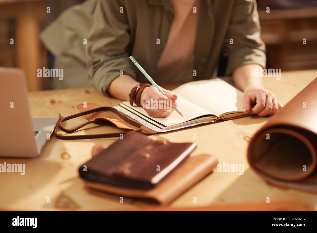 Horizontal shot of unrecognizable woman wearing casual clothes sitting at table making notes in handmade notebook Stock Photo