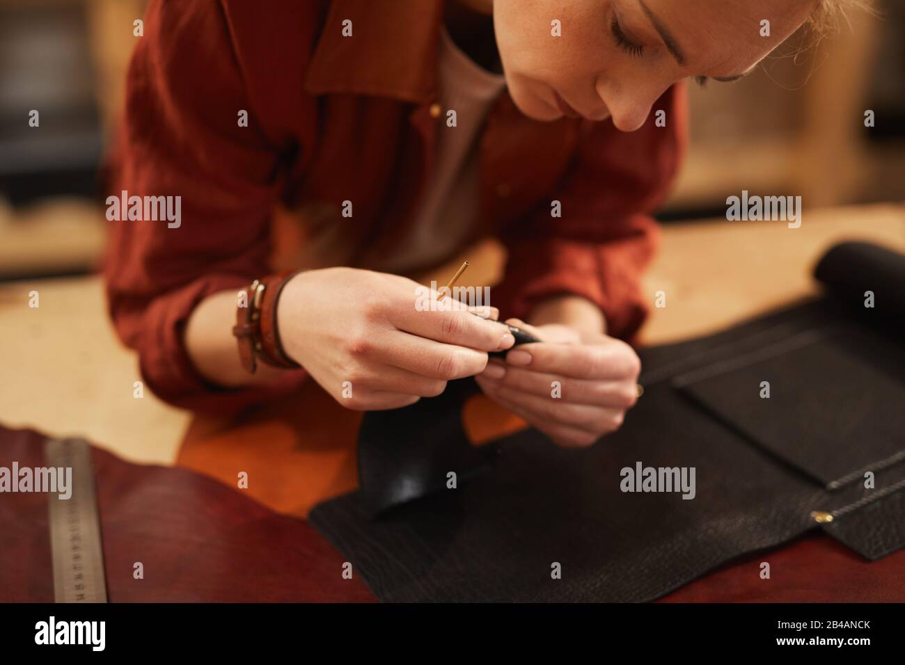 Horizontal shot of young female artisan creating something using leather materials of different colours Stock Photo