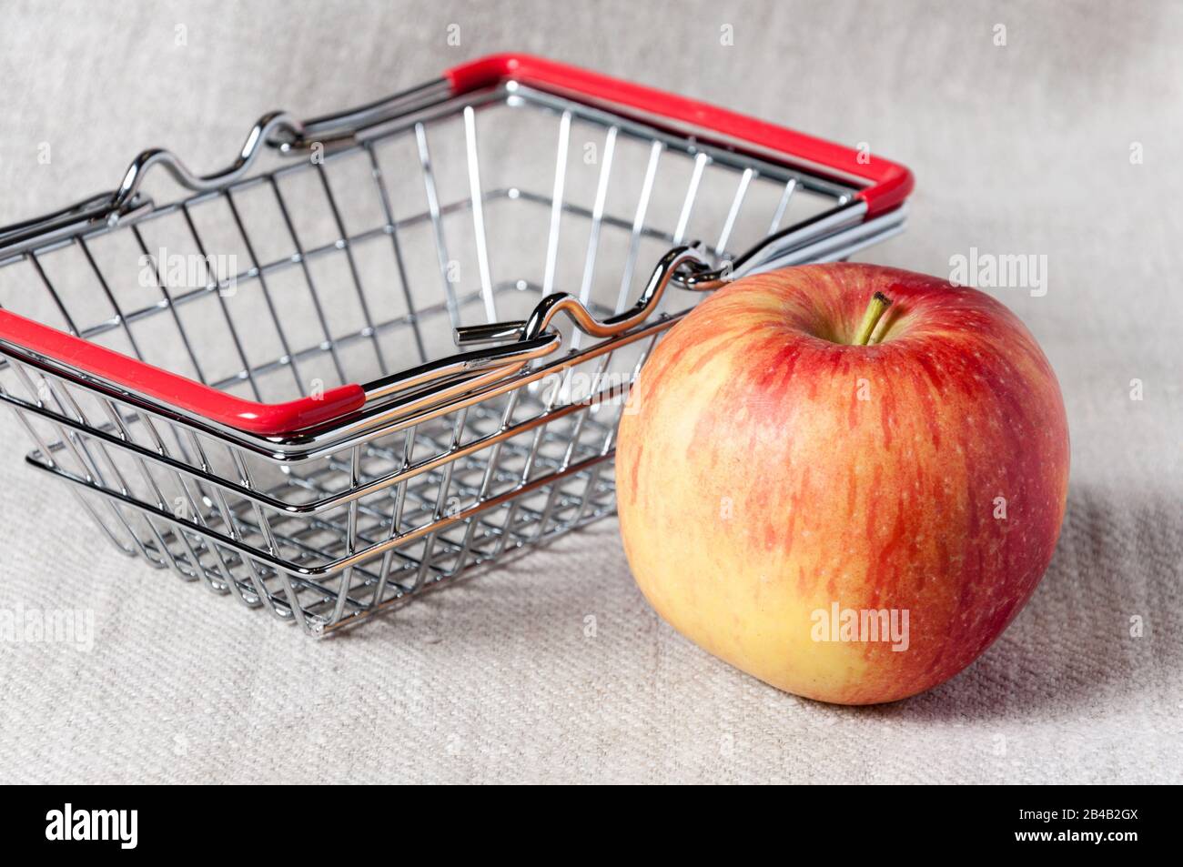 Red apple near a small shopping basket. Miniature shopping basket on