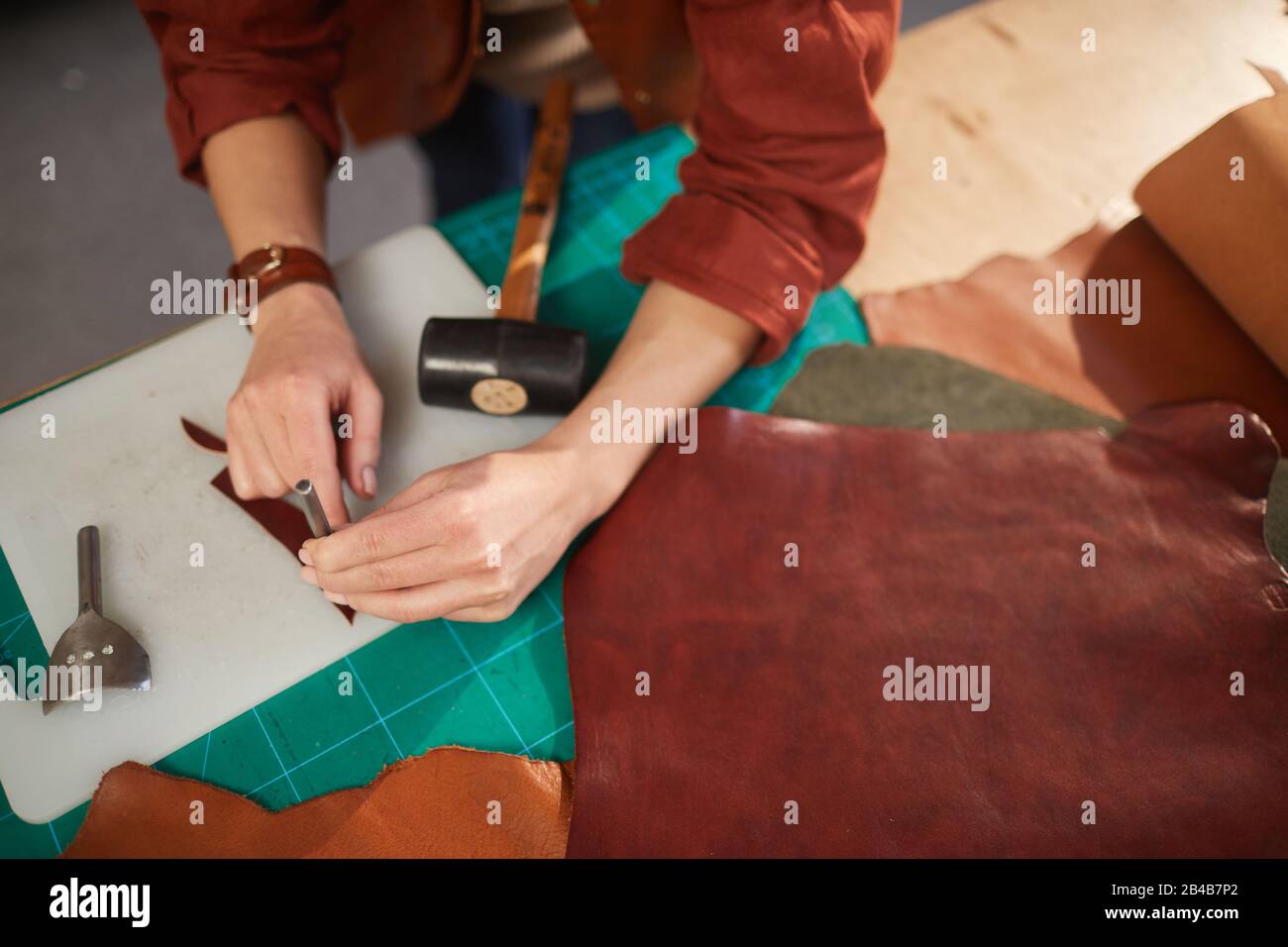 Horizontal from above shot of unrecognizable female artisan using leater punching tool on small detail Stock Photo