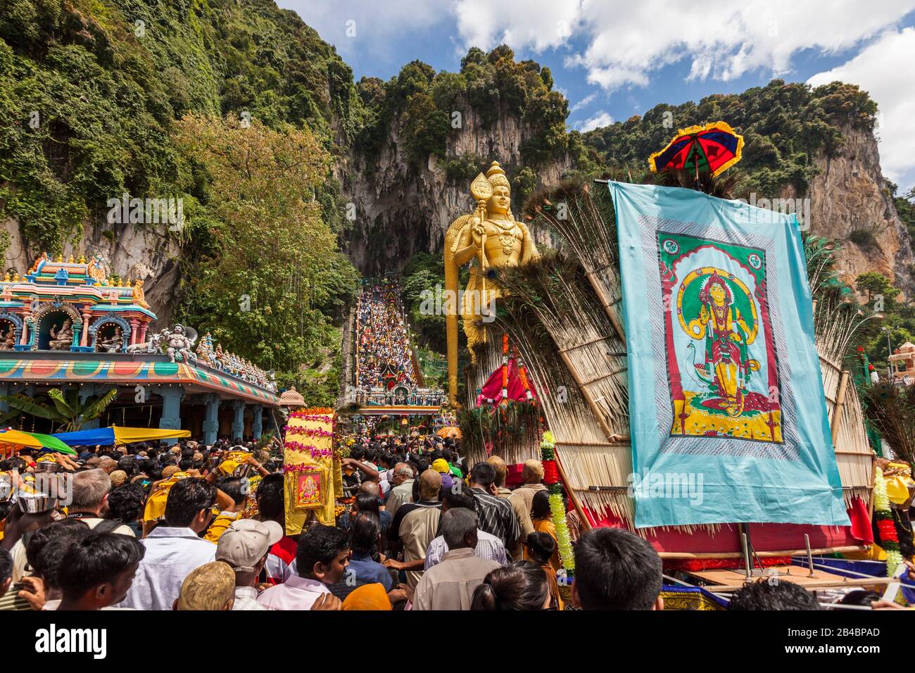 Malaysia, Selangor State, Batu Caves, Hindu festival Thaipusam procession, celebration of god Murugan, son of Shiva and Parvati, crowd of pilgrims walking up the stairs and giant golden statue of God Murugan, big kavadi decorated with peacock feathers in the foreground Stock Photo