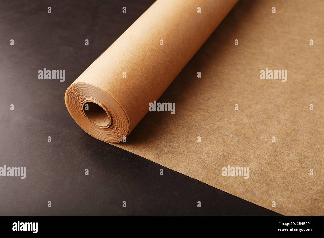 A roll of unfolded brown parchment paper, for baking food in on a dark background, top view