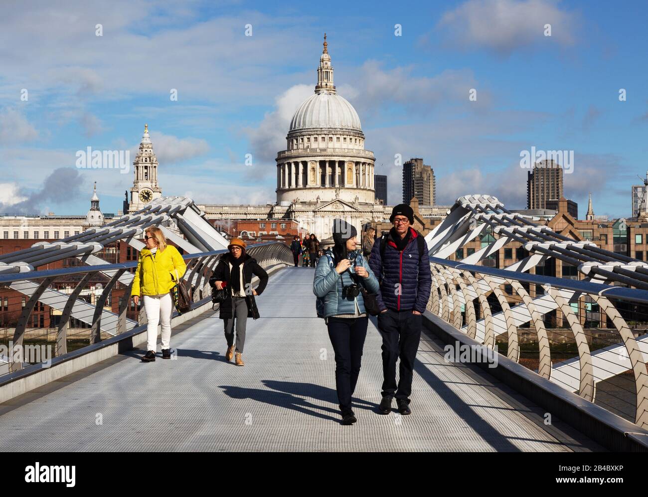 London tourists crossing the Millennium Bridge in front of St Pauls Cathedral on a sunny day in March, London city centre, London England UK Stock Photo