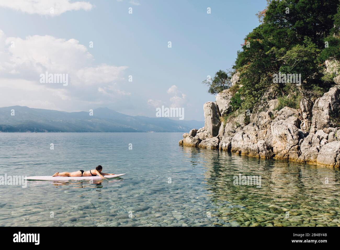Junge Frau liegt auf Surbrett und paddelt im Wasser herum,Cres, Kroatien; Stock Photo