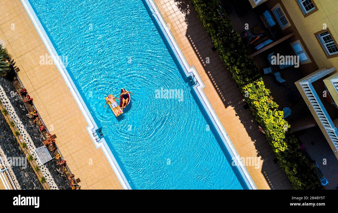 Top vertical view of swimming pool in hotel residence vacation with people adult senior lay down and enjoy with inflatables lilos mattress on blue water - alternative lifestyle for summer vibes Stock Photo