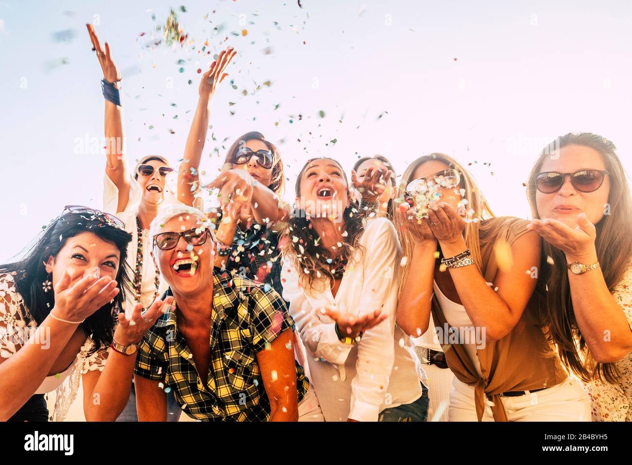 People having fun in party celebration friends concept - group of young and adult women all together laughing blowing coloured confetti - friendship and love for lifestyle with mixed active generations Stock Photo