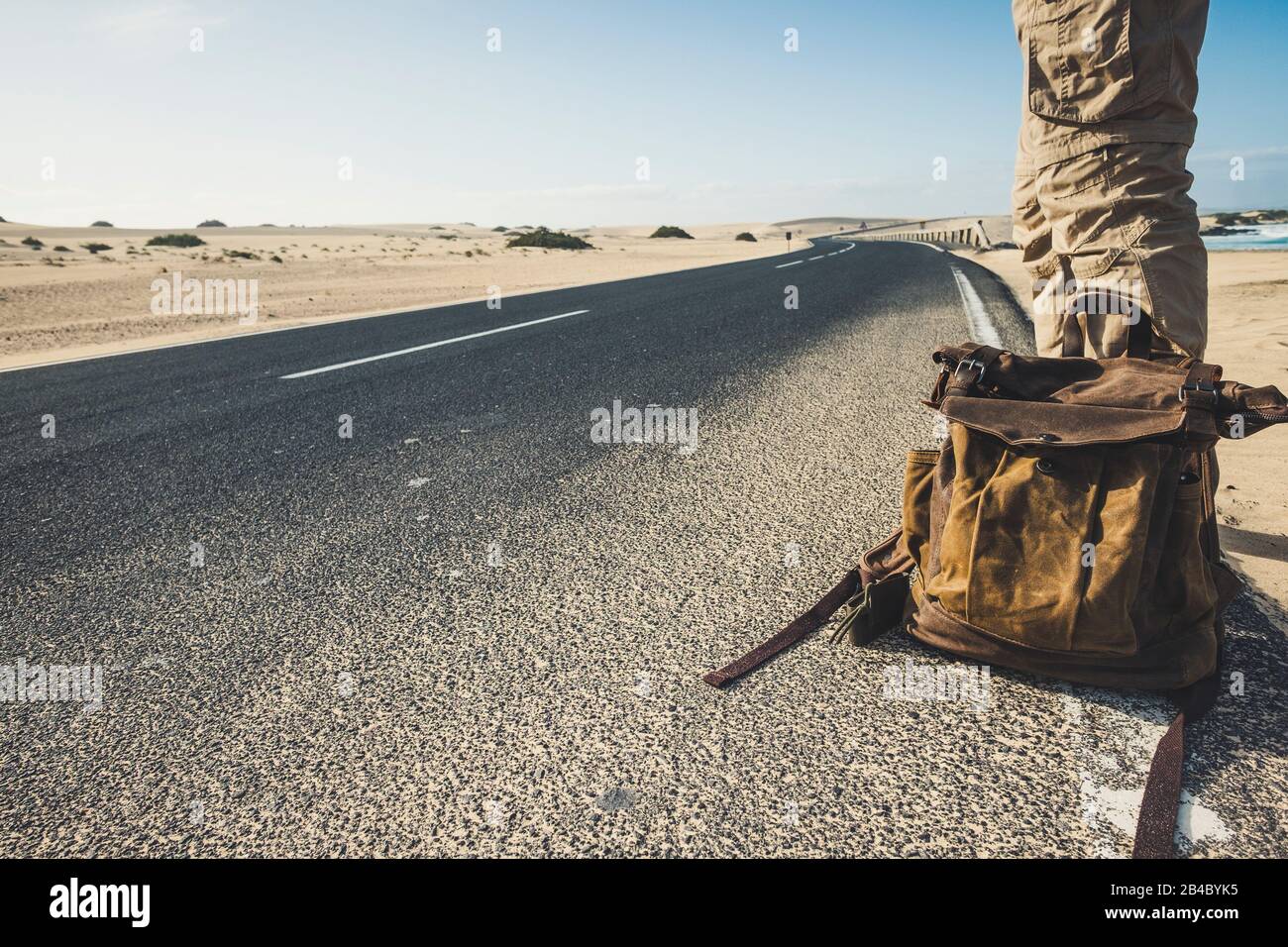 Travel people and adventure lifestyle concept with closeup of man standing on the long road with trendy backpack waiting for a car to share the trip - beautiful desert natural outdoor around Stock Photo