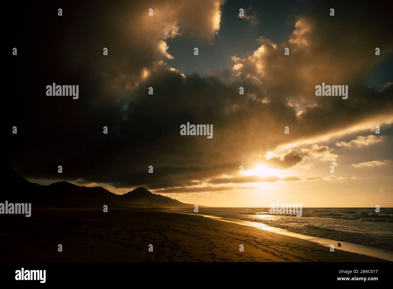 Dramatic dark shadows sunset at the beach with black mountains in background - sun and ocean for adventure concept - scenic landscape and beautiful sky with clouds Stock Photo