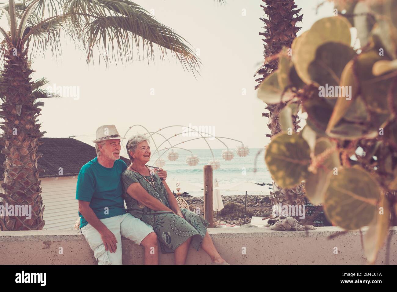 Happy senior adult caucasian people couple sitting and enojying outdoor leisure activity together hugged - forever life concept - vacation sea in background Stock Photo