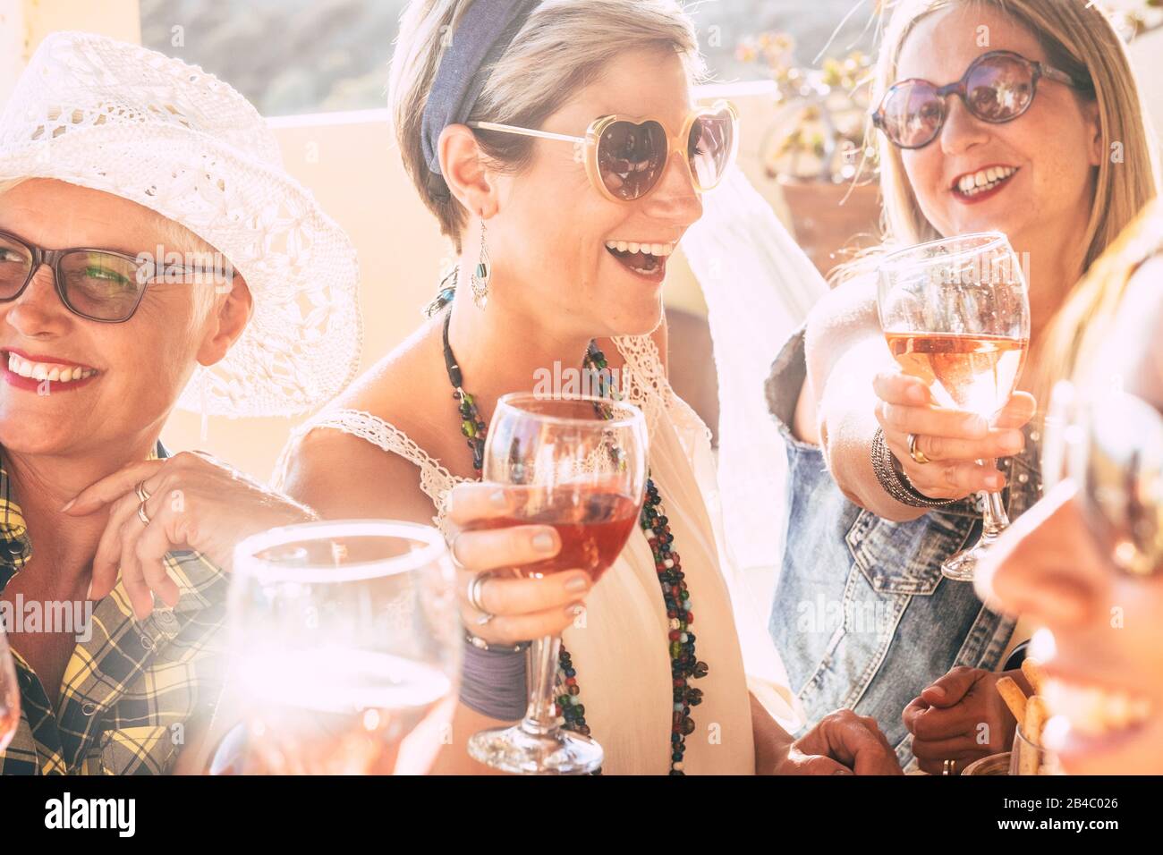 Closeup of happy beautiful cheerful people women celebrating together with red wine - bright sunny image joyful and friendship - young senior ladies smiling and laughing having fun at party Stock Photo