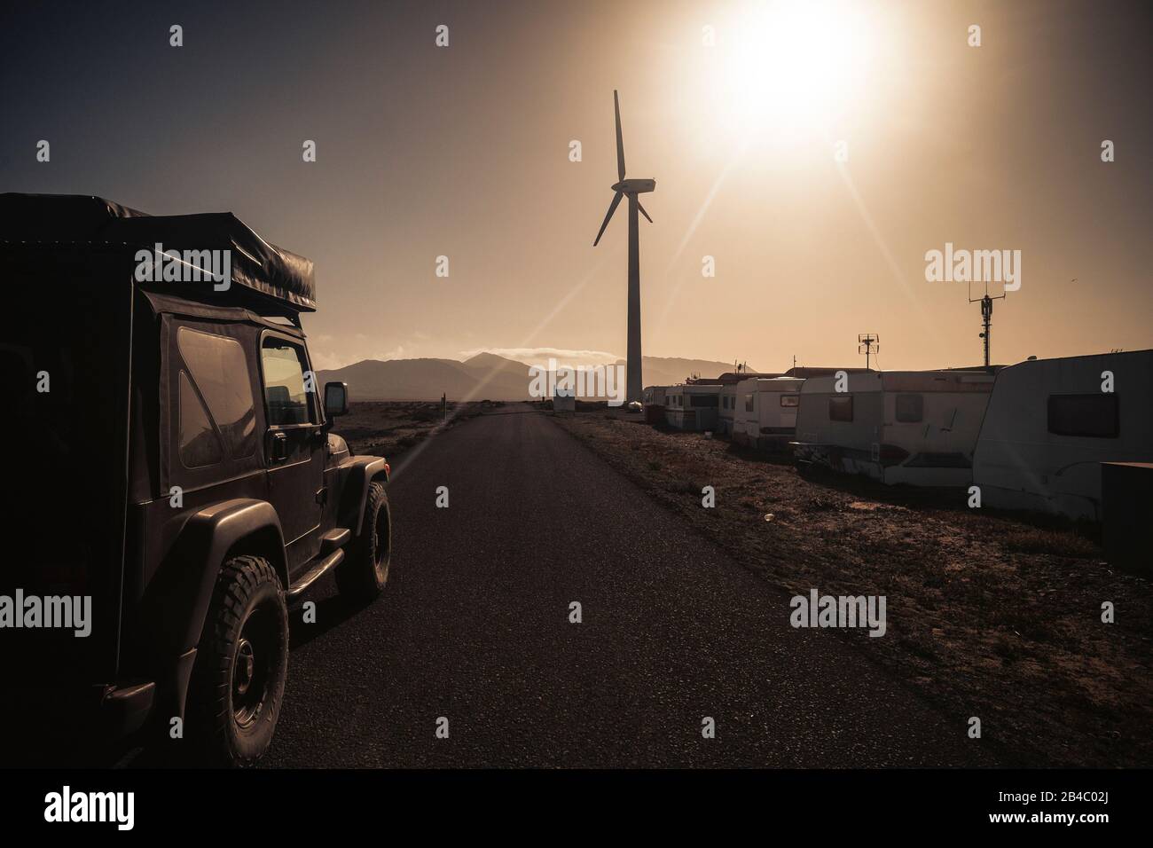 Long way road with black off road 4x4 car with tent ot the roof - scenic landscape for travel adventure wild concept and different vacation lifestyle - sun and sunlight with warm sky Stock Photo