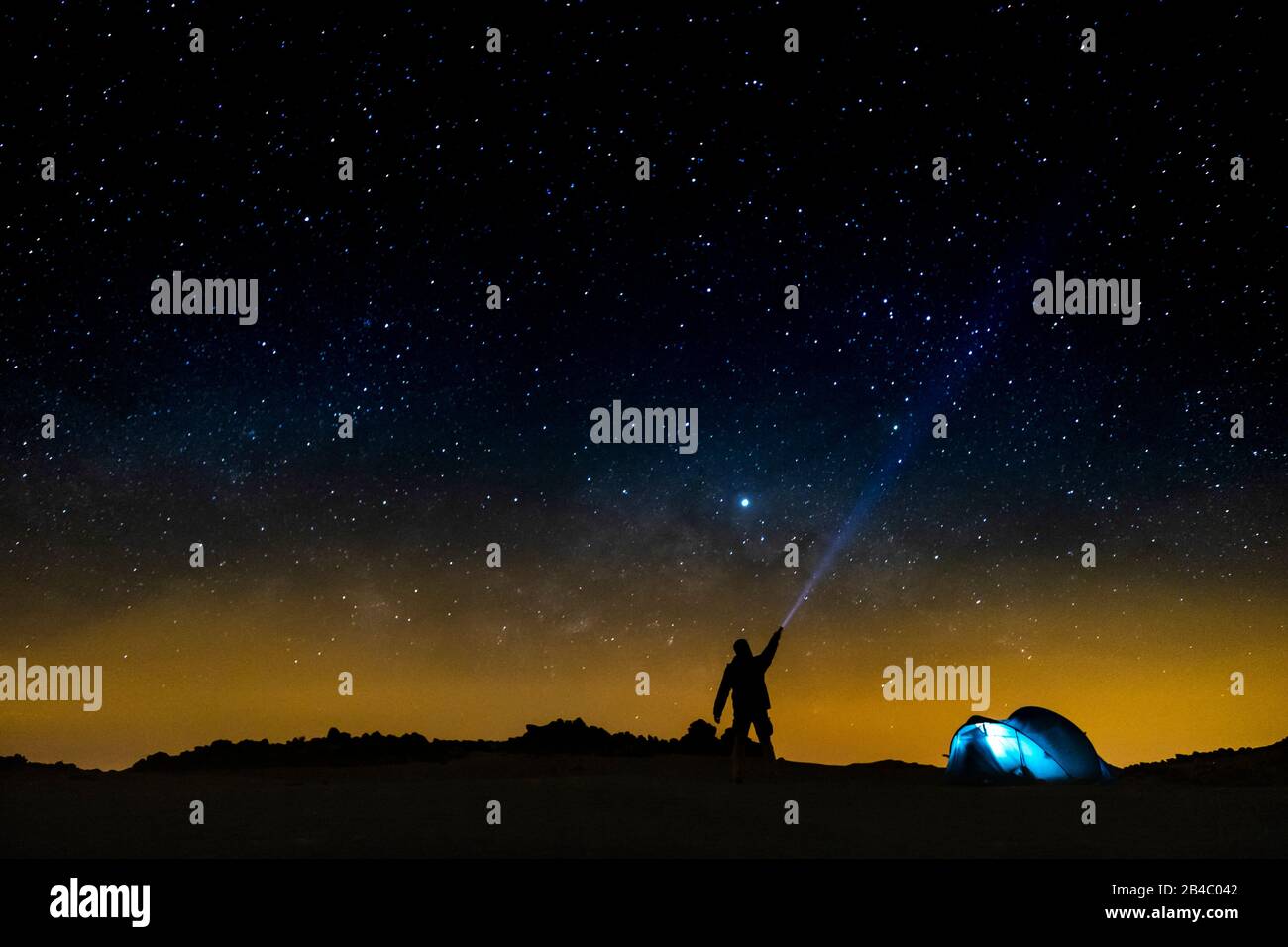 Night sky with stars and silhouette of a standing happy man with blue light. Space background - travel people concept - free camping and outdoor adventure - discover the world lifestyle Stock Photo