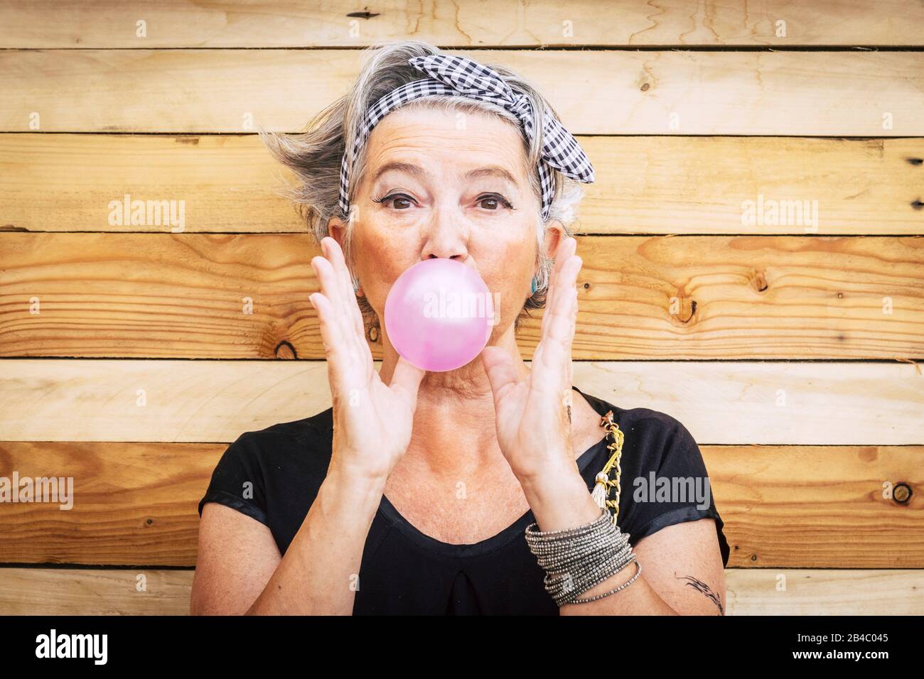 Funny and alternative old people caucasian beautiful woman with pink bubble chewing gum - portrait of youth active senior lady having fun - no limit age lifestyle concept Stock Photo