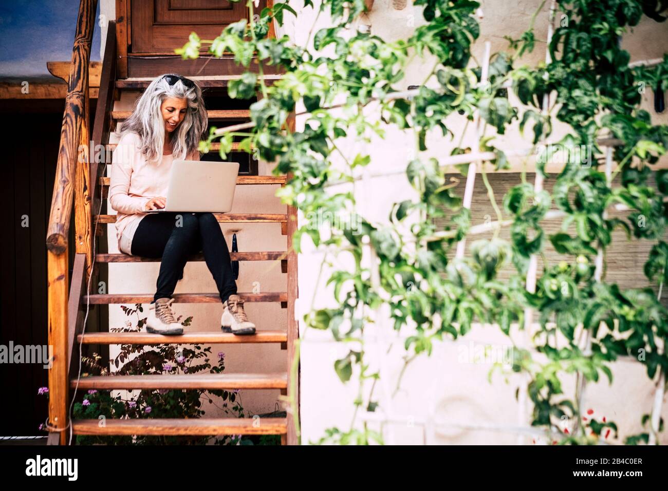 Adult alternative diversity people concept white and grey long hair beautiful woman with laptop computer sitting on a wooden stairs outside home - happy free people with internet technology everywhere Stock Photo