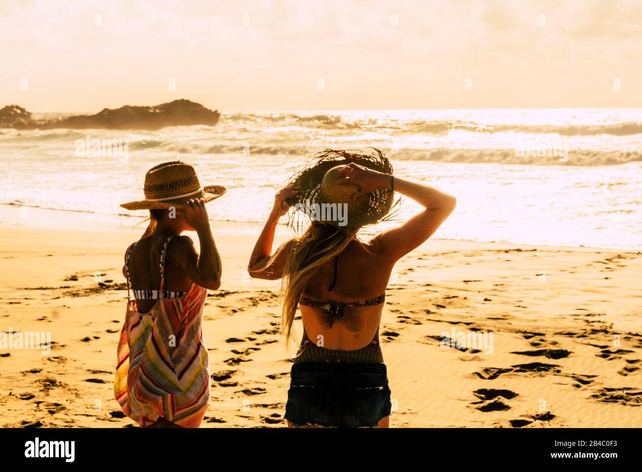Sunset light at the beach with people enjoying the outdoor holiday vacation leisure - couple of women friends enjoying the nature in tropical scenic place - golden colors and freedom concept Stock Photo
