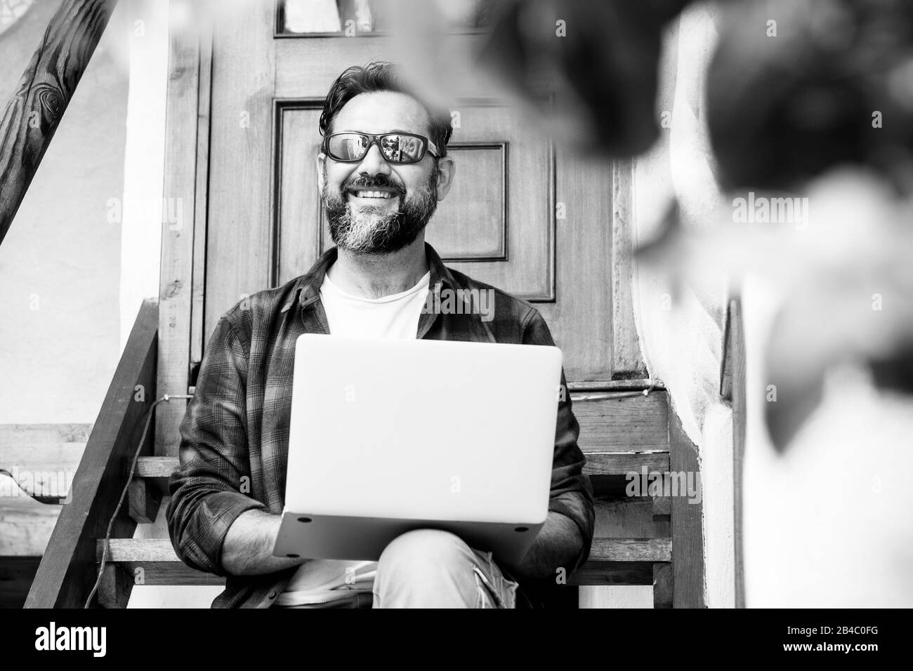 Black and white portrait of cheerful adult man working outdoor at home with personal notebook laptop computer - internet connection for free people concept Stock Photo