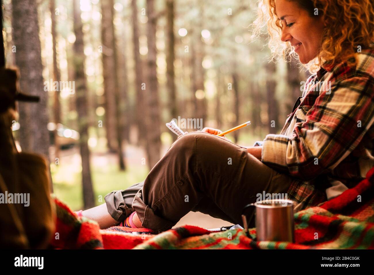 Travel alternative and wanderlust lifestyle people - beautiful young woman sit down ina tent with scenic forest outdoor in background - adventure and environment concept for free hipster female Stock Photo