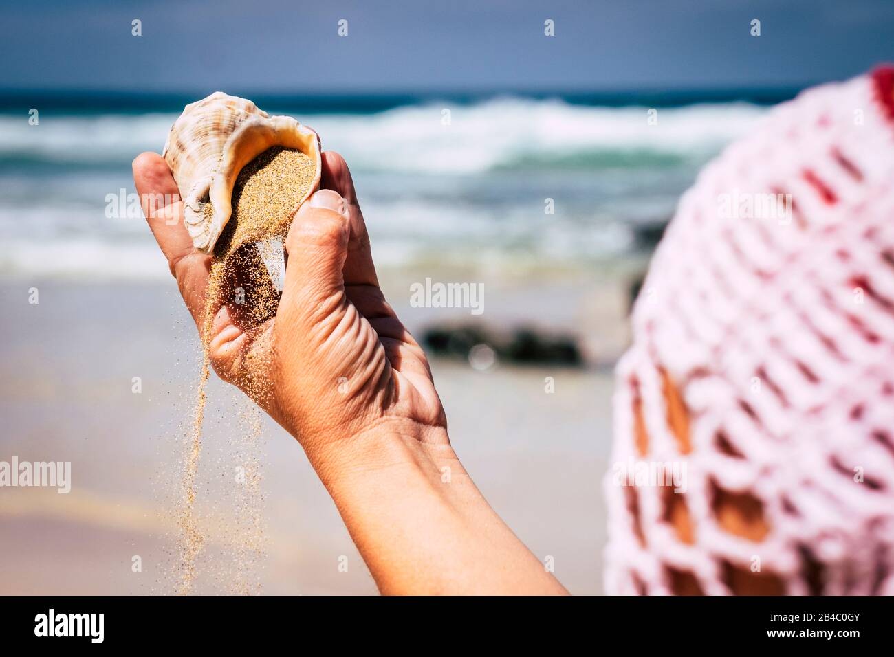 Nature and environment concept with close up of woman hands with shell and sand - travel and holiday summer vacation at the beach - blue sea and waves in background Stock Photo