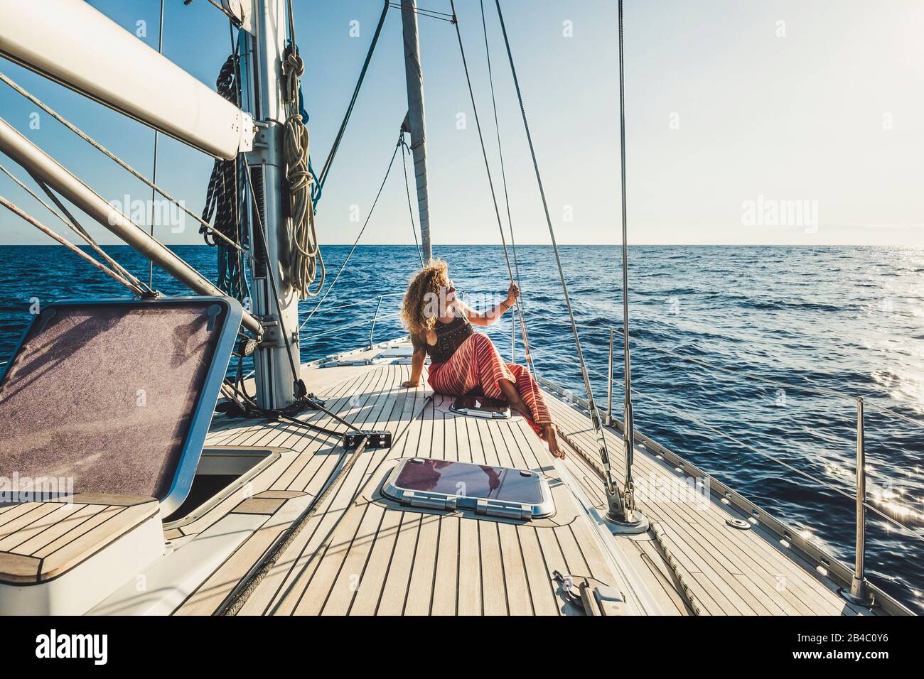 People enjoy travel adventure with alternative transportation way - beautiful curly blonde woman sit down on a sail boat with ocean and sky around - enjoying holiday vacation and luxury lifestyle Stock Photo