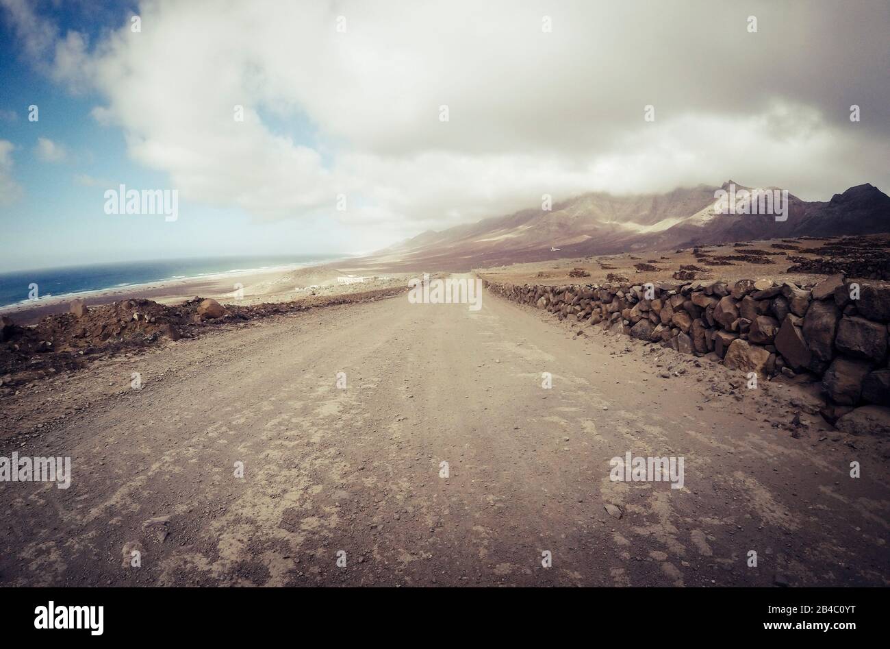 Long off road terrain way road viewed from ground level with mountains and coastline ocean view - travel and adventure concept for alternative vacation and lifestyle Stock Photo