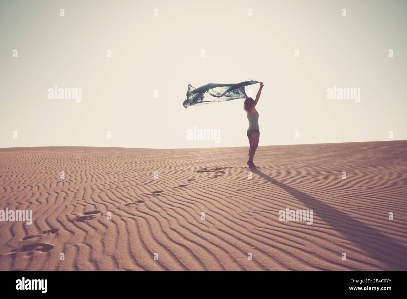 Freedom and happiness concept with standing lady in the dunes sandy desert enjoying the nature oudoor with clear white sky in background - travel destination concept - brown colors filter Stock Photo