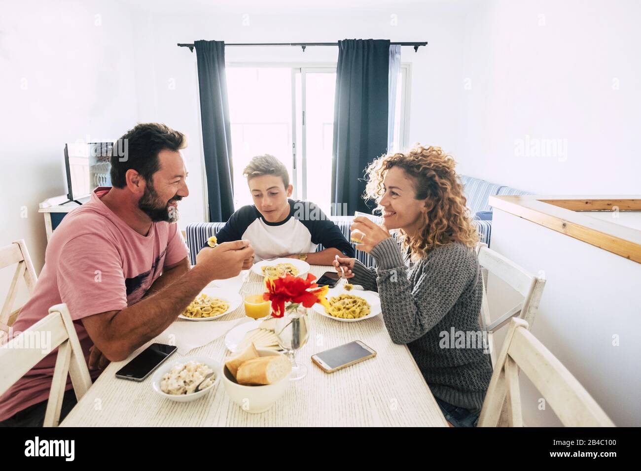 Cheerful people smiling happy family have lunch together at home - white backgorund and mother father and teenager son eating italian pasta enjoying the life together Stock Photo