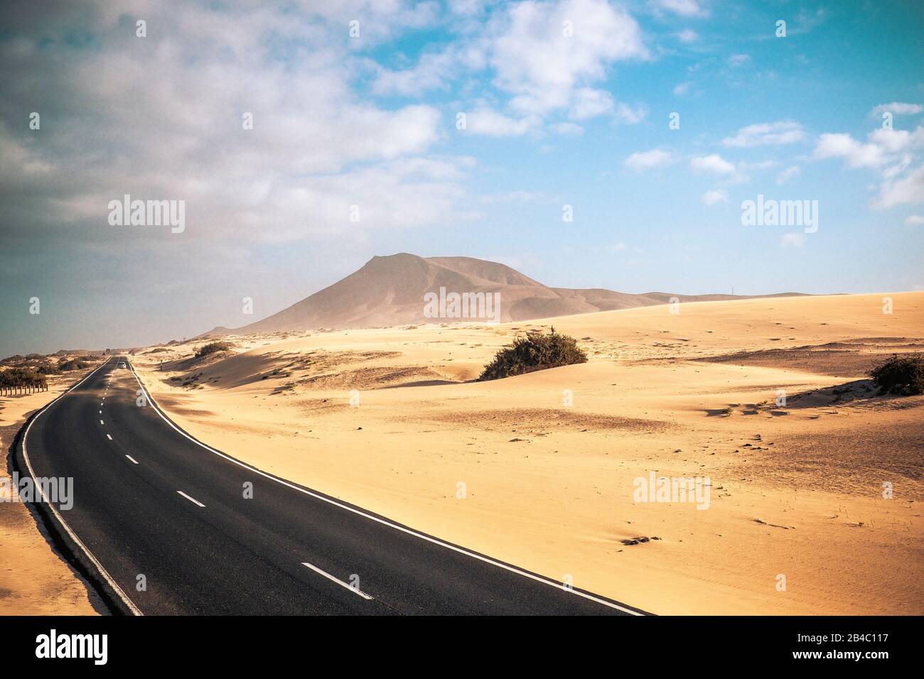 Travel on the road concept with long way asphalt road in the middle of the dunes sandy desert and mountains for adventure and alternative scenic places for vacation or adventure lifestyle experience Stock Photo