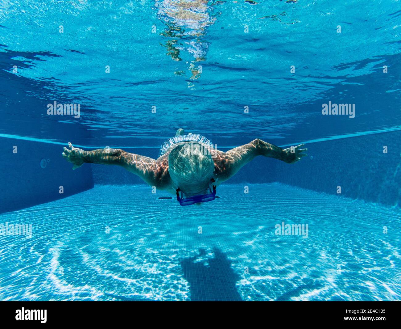 Active people old senior man swimming underwater on a blue pool water