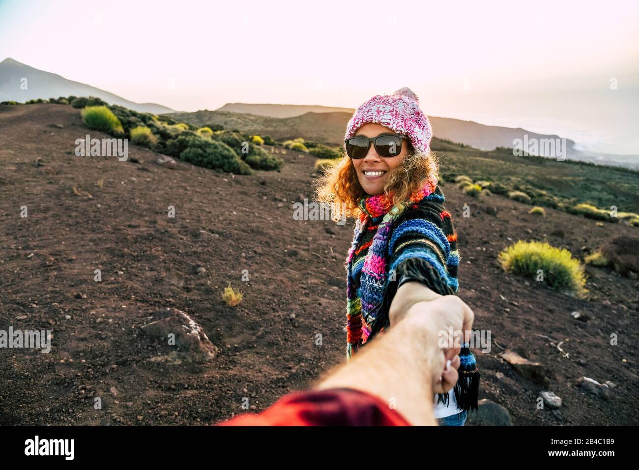 Beautiful cheerful adult young woman smile and holding man hand during outdoor leisure activity trekking at the mountain - travel couple concept for active people - freedom holiday vacation in the nature Stock Photo