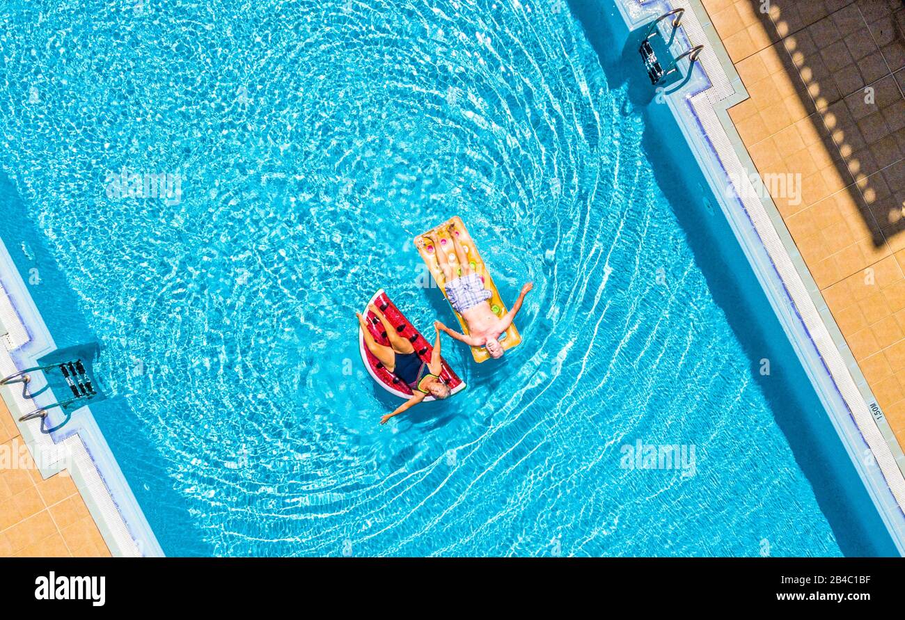 Aerial top vertical view of people old senior couple enjoying the retired lifestyle lay down with trendy coloured lilos inflatable mattress on a blue water clear swimming pool in resort hotel summer vacation Stock Photo