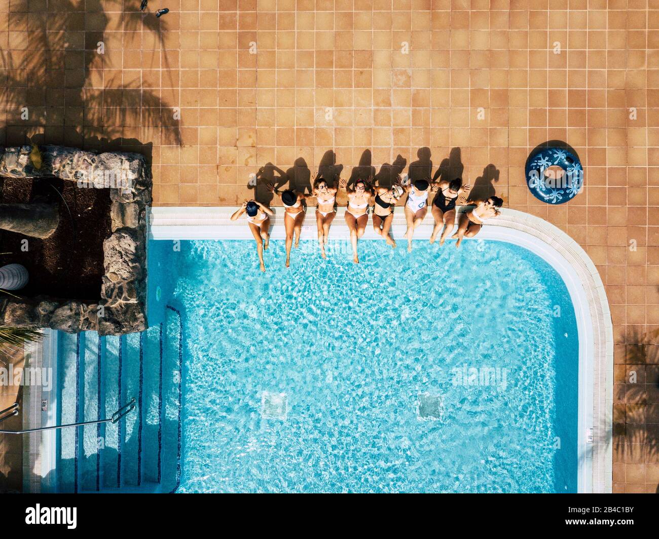 Friends females caucasian people enjoying the swimming pool in summer holiday vacation at hotel or resort - high top vertical view of young women sit down at the poolside in friendship together Stock Photo