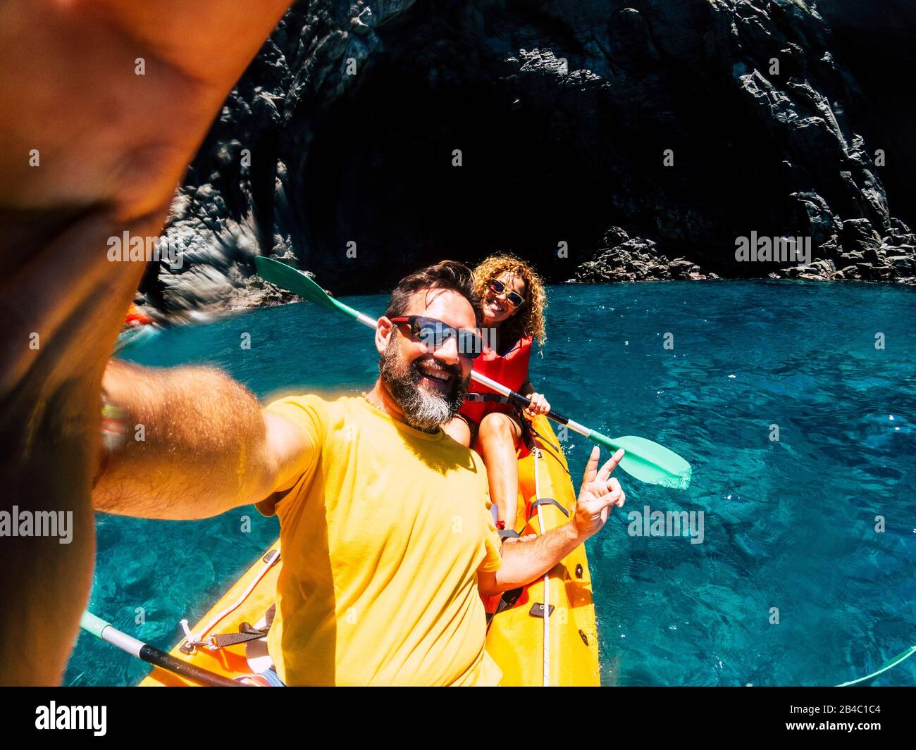 Happy cheerful people enjoying outdoor leisure activity in kayak on the coast ocean - selfie picture with nice couple - cave and ocean background and colors for vacation summer concept Stock Photo