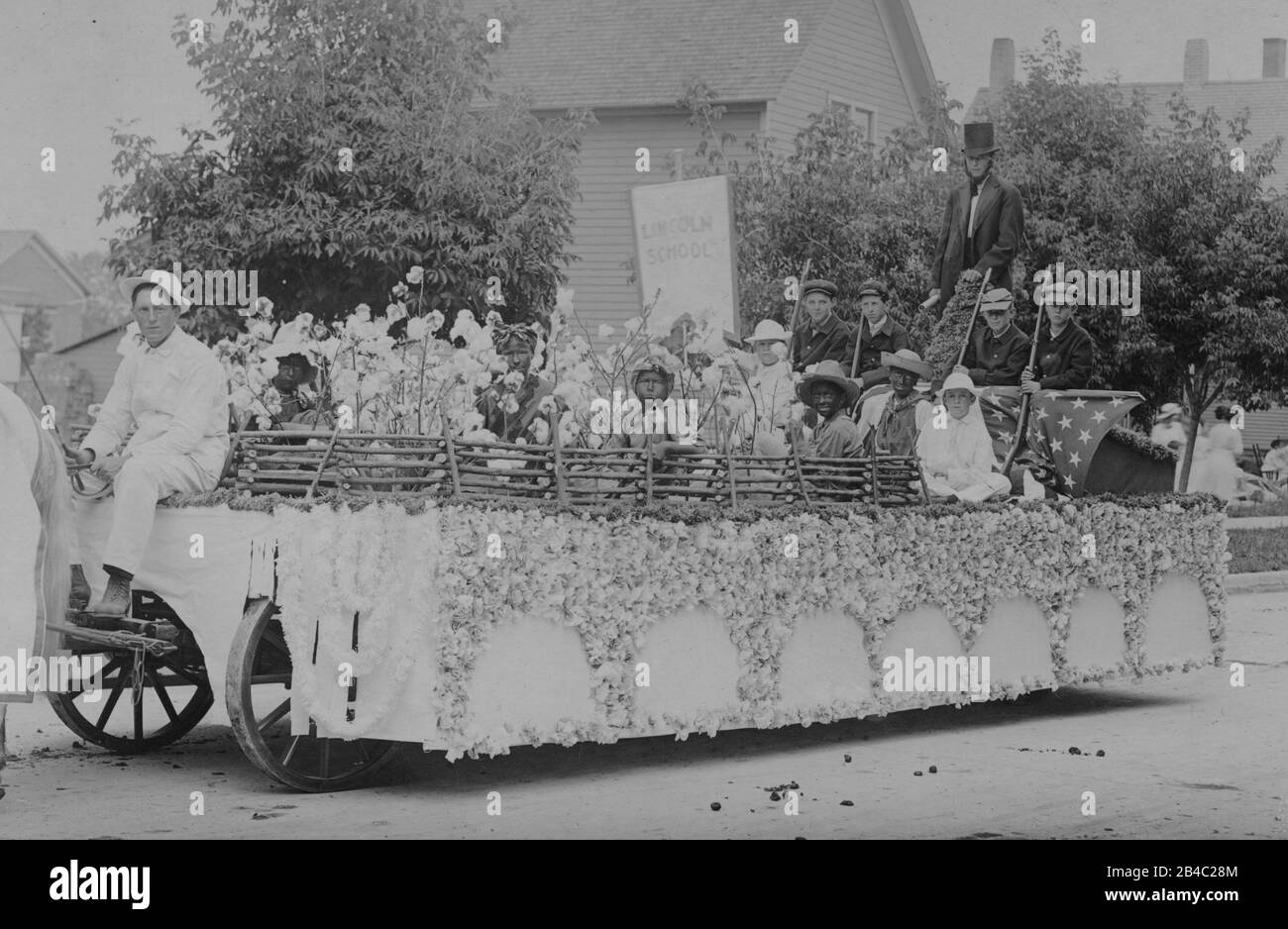 Racist  Parade float of Blackface and White children sitting in a thick Cotton field on a flatbed farm wagon, c. 1915. All around the field and kids is an imitation split rail fence. Other boys, dressed as soldiers armed with Civil War-era musket rifles watch over them. A man dressed as top-hatted President Abe Lincoln stands in back, holding a scrolled paper. Behind the kids and cotton is a tall white banner, weakly printed with 'Lincoln School'  All these folks and the location are unknown.  To see my related vintage images, Search:  Prestor  vintage  African Stock Photo
