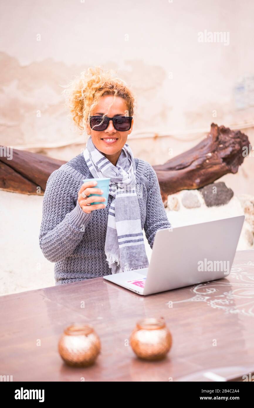 Woman outdoor with technology personal laptop computer smile at the camera and drink a coffee - alternative natural office workstation for modern digital nomad people traveling the world Stock Photo