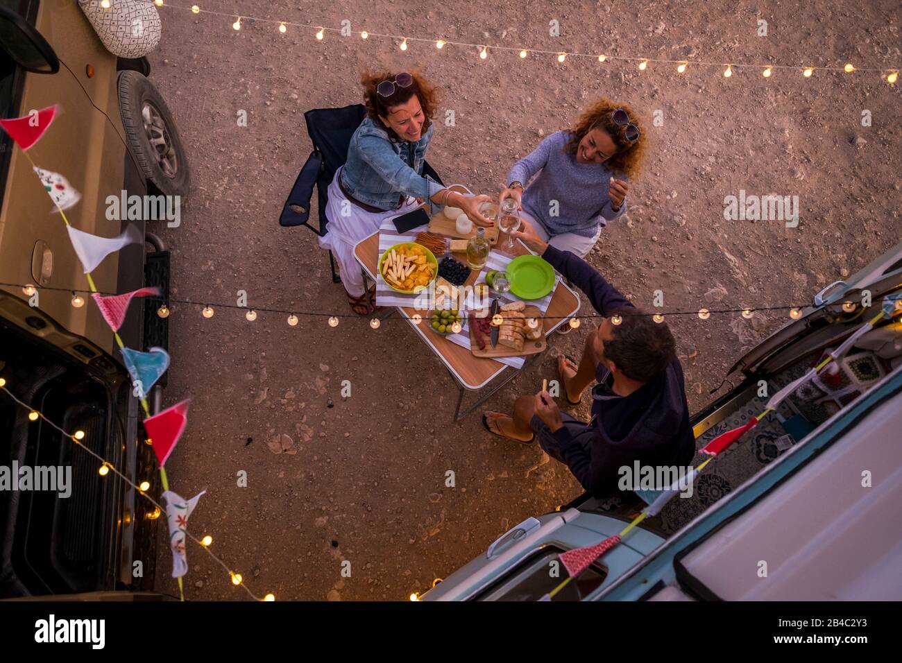Group of friends having dinner together in friendship outside little van - alternative travel lifestyle and vehicle vacation - people having fun and enjoy the freedom and the adventure - vertical view Stock Photo