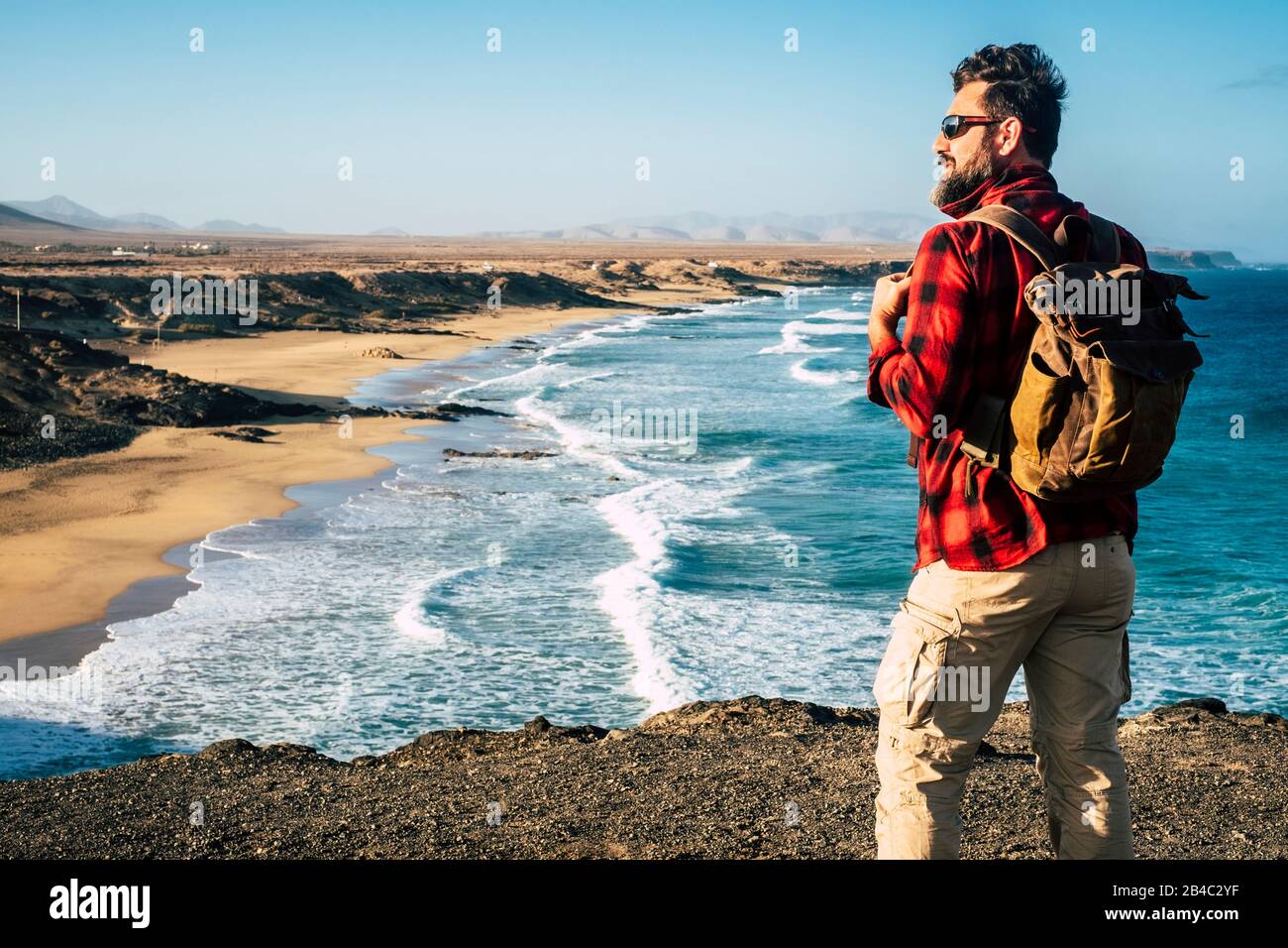 Standing man traveler people look and enjoy the destination on a wonderful tropical beach with rock cliff - alternative vacation lifestyle - wanderlust and backpack life Stock Photo