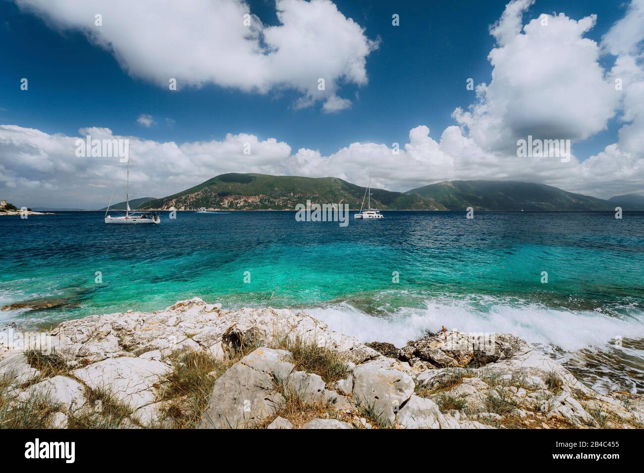 Crystal clear transparent blue turquoise teal Mediterranean sea water in Fiskardo town. White yacht in open sea at anchor under amazing white clouds, Kefalonia, Ionian islands, Greece. Stock Photo