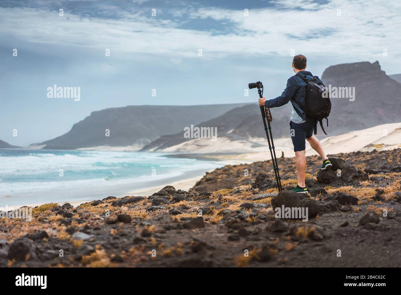 Photographer with camera on tripod in desert admitting unique landscape of sand dunes volcanic cliffs on the Atlantic coast. Baia Das Gatas, near Calhau, Sao Vicente Island Cape Verde. Stock Photo