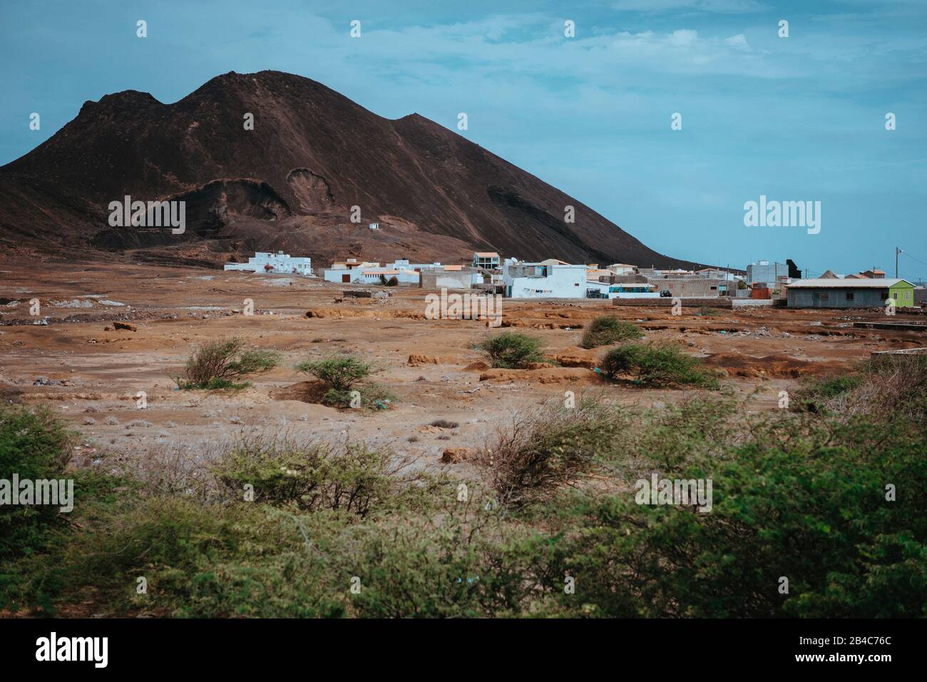 Local dwelling in front of Calhau volcanic crater, Cape Verde - Sao Vicente Island. Single martian like dry red rock stand out from barren desert ground. Stock Photo