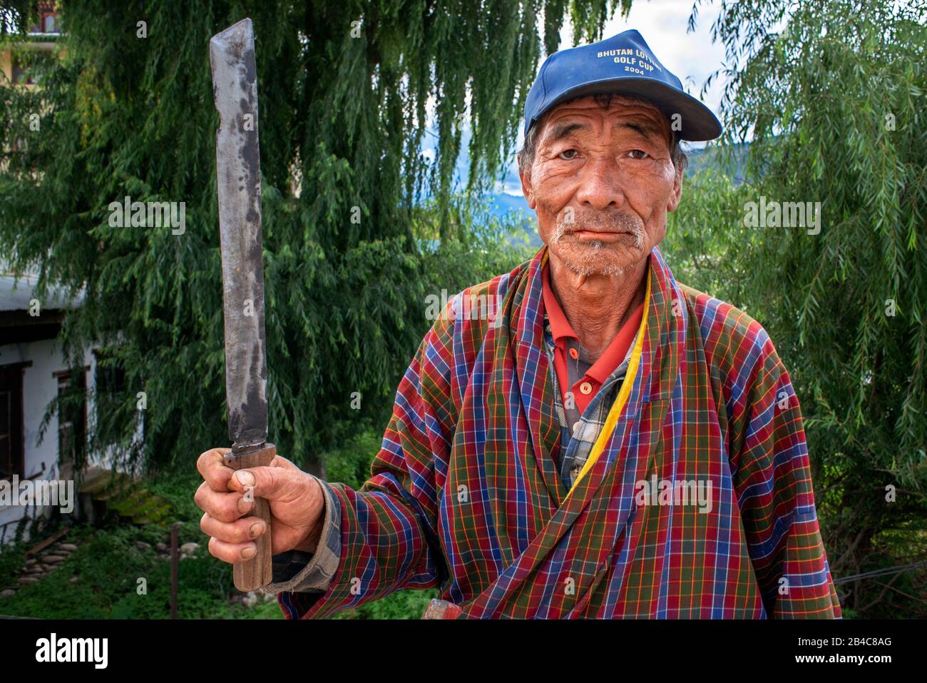 Portrait of a farmer with a knife in Paro Valley with Rice Paddies Farming Animals near Paro Chhu River Bhutan. Stock Photo