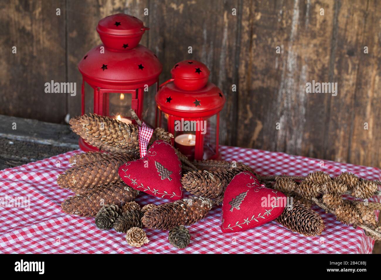 rustic Christmas still life with red lantern, fabric hearts and pine cones across an old wooden wall Stock Photo