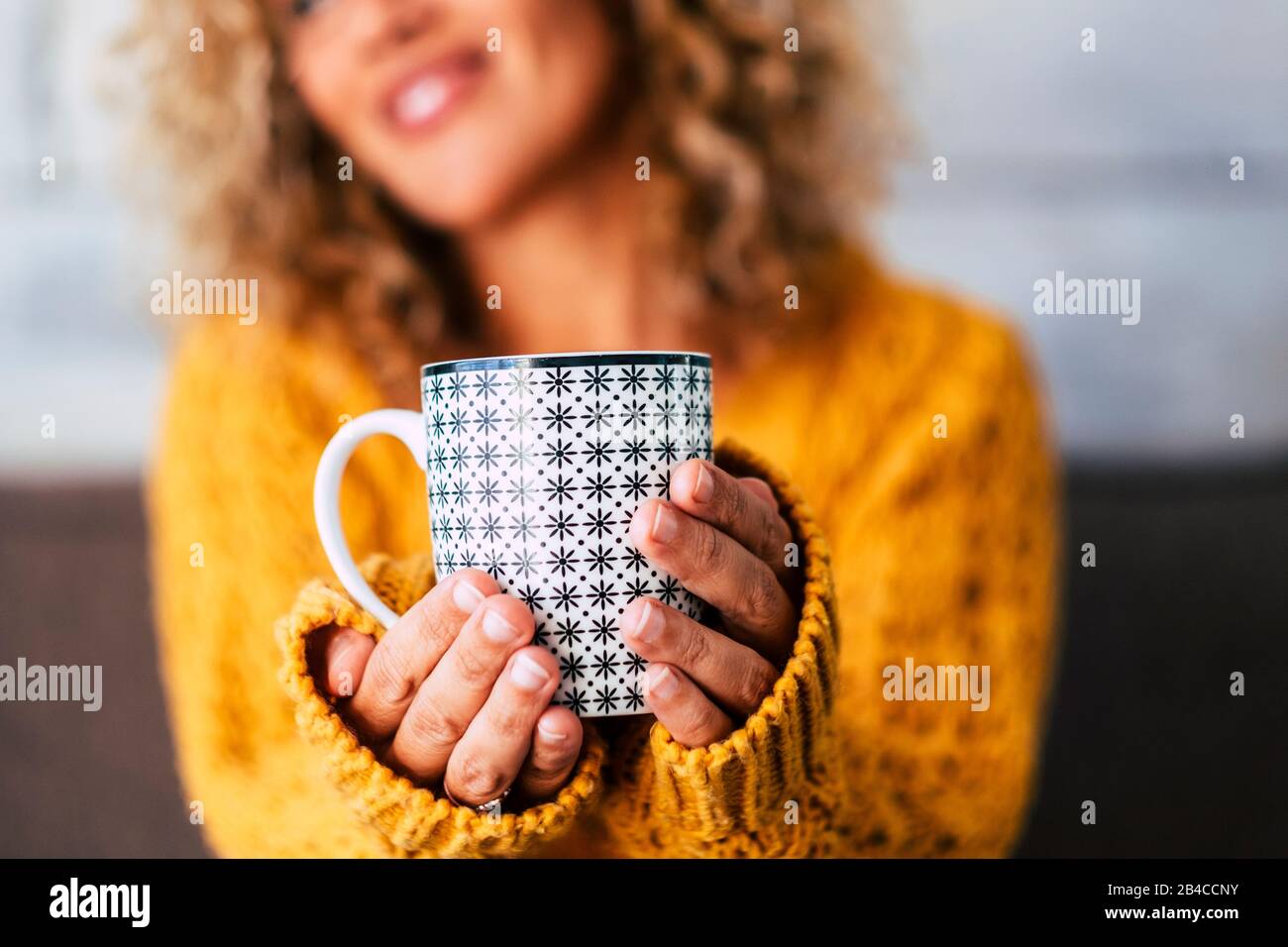 Close up of design trendy mug with tea or coffee or heahty drink holded by adult caucasian woman hands -  cheerful blonde female people in background defocused Stock Photo