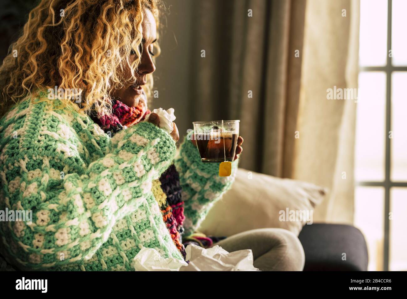 Adult beautiful caucasian woman at home sick with ill and cold drinking hot tea - fever and seasonal influenza illness concept for unhealthy people sitting and taking medicine Stock Photo